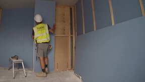 Boarder tacking plasterboard sheet to the wooden frame in the workplace