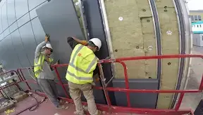 Two rainscreen cladders installing a cladding panel on the external wall