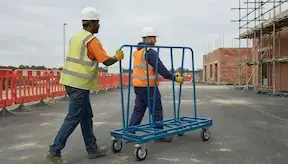 Two site operatives/labourers moving a-frame trolley accross the construction site